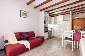 A red sofa, white dining table, and kitchen area with cabinets and appliances.