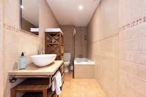 A bathroom with a wooden vanity, a large white basin, a toilet, and a bathtub.