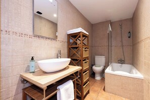 A bathroom with a large white sink, a wooden vanity, a toilet, and a bathtub.