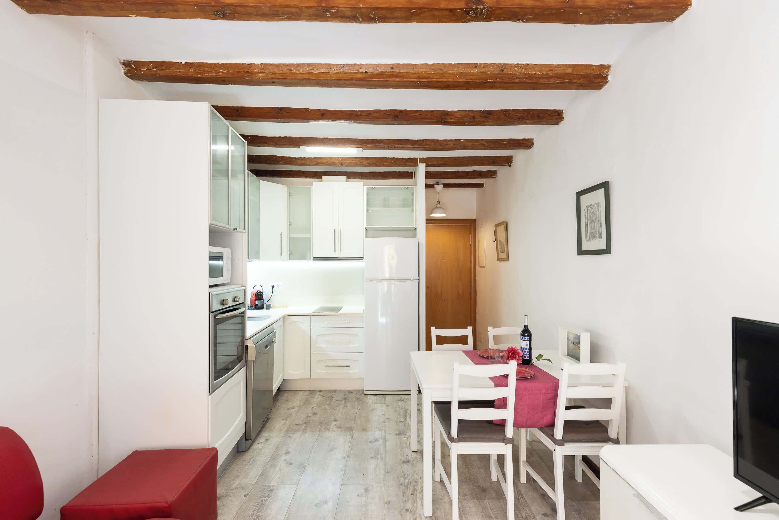 A compact kitchen with white appliances, a dining area with a table and chairs, and a television.