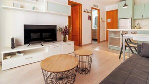 A modern living room with a TV, white entertainment unit, two wooden tables, and a sofa. - Ripoll Old Town - Unik Vacation (Tarragona)