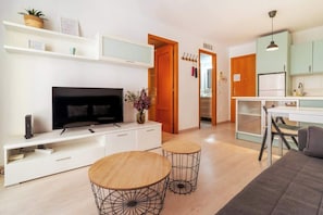Una sala de estar moderna con televisor, mueble blanco para entretenimiento, dos mesas de madera y un sofá.