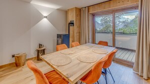 A dining area with a wooden table, orange chairs, and a view of a mountainous landscape through large windows.