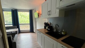 Pieni, käytännöllinen keittiö, jossa on valkoiset kaapit, musta pesuallas ja sinisillä verhoilla varustettu ikkuna.