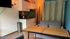 Kompakti oleskelutila, jossa on sohva, ruokapöytä, pieni keittiö ja seinälle asennettu televisio.