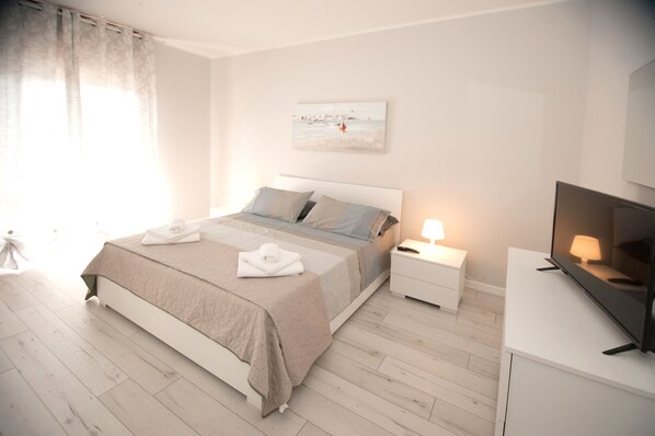 Ein modernes Schlafzimmer mit Bett, Nachttischen, einem Fernseher und einem Bild an der Wand.