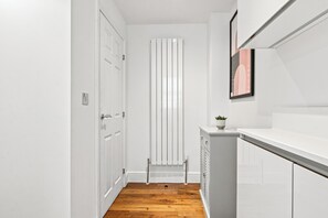 A narrow hallway with wooden flooring, white walls, a radiator, and a door with a light switch.