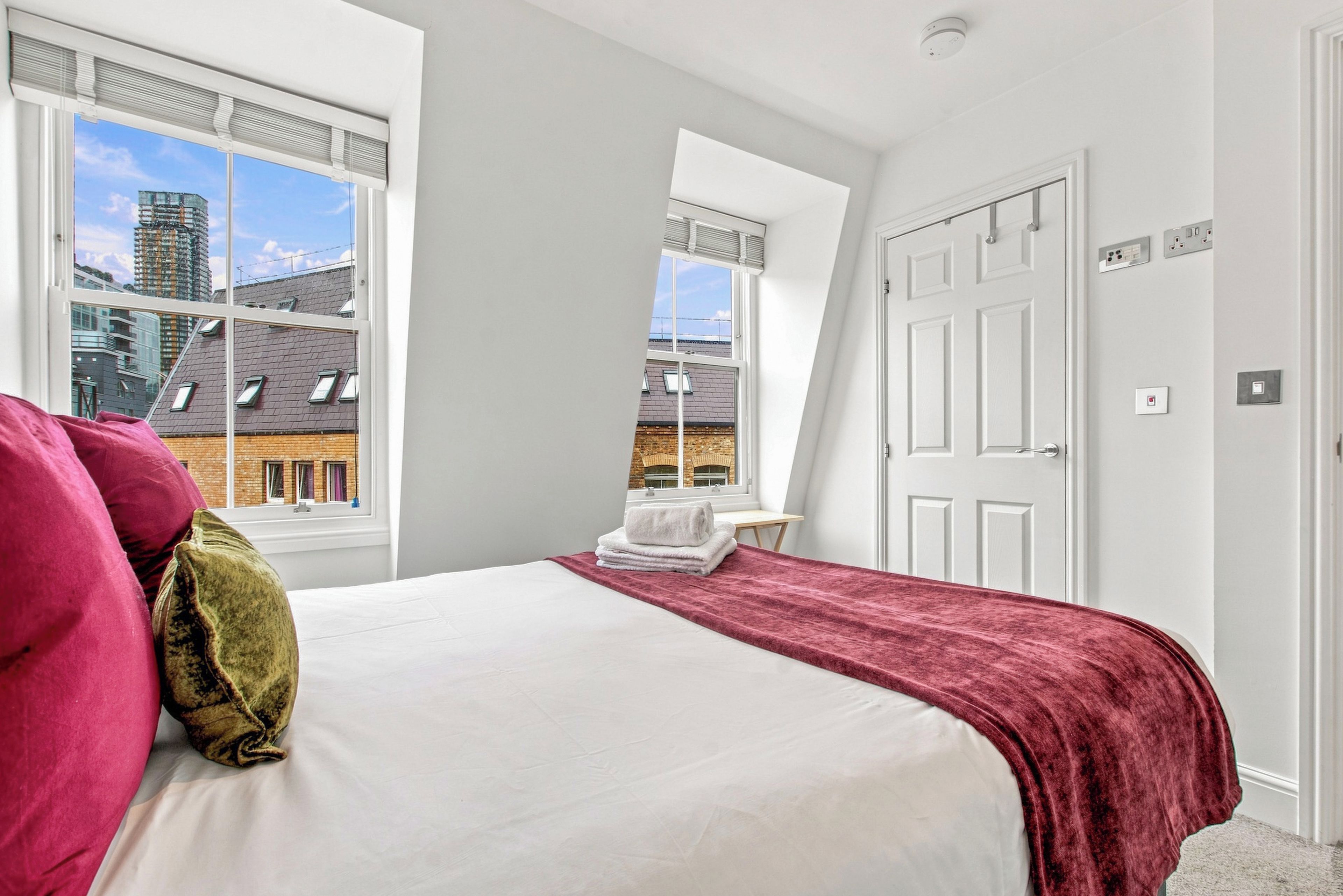 Een slaapkamer met een bed, een raam, een deur en uitzicht op gebouwen.
