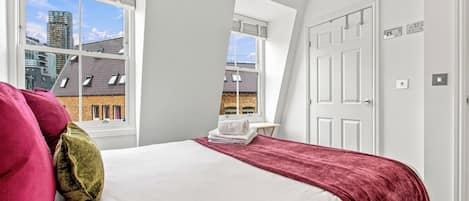 Un dormitorio con cama, ventana, puerta y vistas a edificios.