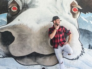 A person sitting on a wall with a large, colorful mural of a cow's face.