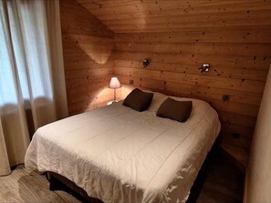 A wooden-paneled room with a bed, a lamp, and a window with curtains.