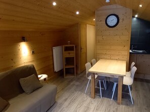 A cozy room with a wooden ceiling, a dining table with chairs, a sofa, a radiator, and a clock on the wall.