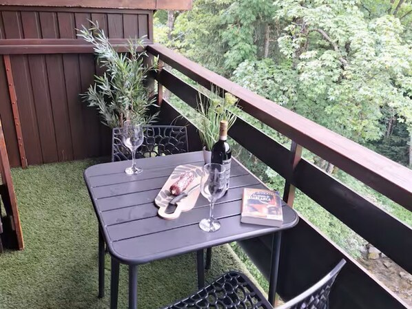 A small outdoor table with a bottle, glasses, and a menu on a balcony with a view of trees.