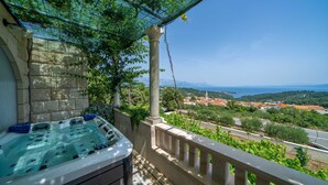 Uma banheira de hidromassagem numa varanda com vista para uma vila costeira e montanhas.