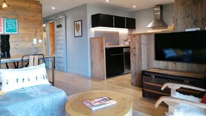 A modern living room with a sofa, a coffee table, a TV, and a kitchen area with wooden cabinets and a dishwasher. - Renovated apartment for 4, near slopes in Pra Loup (Pra-Loup)
