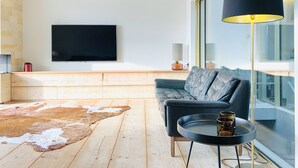 A modern living room with a large flat-screen TV, a dark sofa, a round coffee table, and a large floor lamp. - Beautiful Specious Design Duplex Penthouse With sea View (Knokke-Heist)
