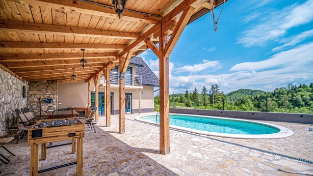 Un espace extérieur abrité comprenant une table de baby-foot, un sol en pierre, une piscine et une vue sur une montagne.