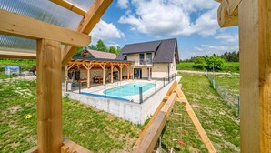 Une maison à deux étages avec une piscine, un patio couvert et un mur en pierre.