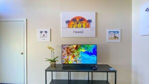 A room with a television on a black stand, a small potted plant, and two framed pictures on the wall labeled 'Hawaii'.