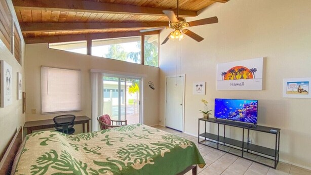 A bedroom with a bed, a television, a ceiling fan, and a window with blinds.