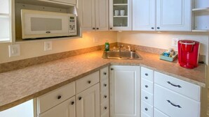 A kitchen with white cabinets, a microwave, a sink, and a red coffee maker.