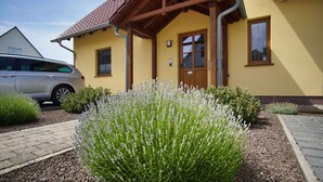 A yellow building with a red-tiled roof, a wooden porch, and a gravel pathway.