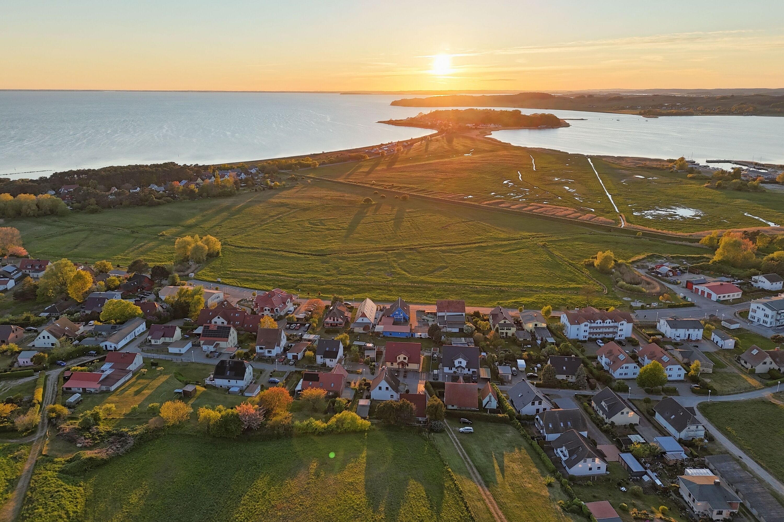 Vue aérienne d’un village côtier avec ses maisons, ses champs et une étendue d’eau.