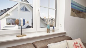 Une pièce avec une fenêtre, un élément de décoration en forme de poisson, un canapé avec des coussins à motifs et un mur orné d’un tableau.