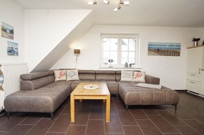 A modern living room with a sectional sofa, a wooden coffee table, a radiator, a window with a view, and a ceiling light fixture.