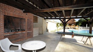 An outdoor patio with a brick barbecue grill, a round table, and a pool area. - Le Clos des Rives Appt N°07 (Saint-Vincent-de-Cosse)
