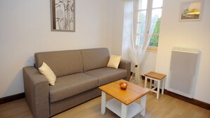 A living room with a sofa, a small wooden table, and a radiator. - Le Clos des Rives Appt N°07 (Saint-Vincent-de-Cosse)