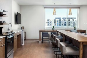 A modern kitchen with a built-in oven, a dining area with bar stools, and a large window offering a city view.