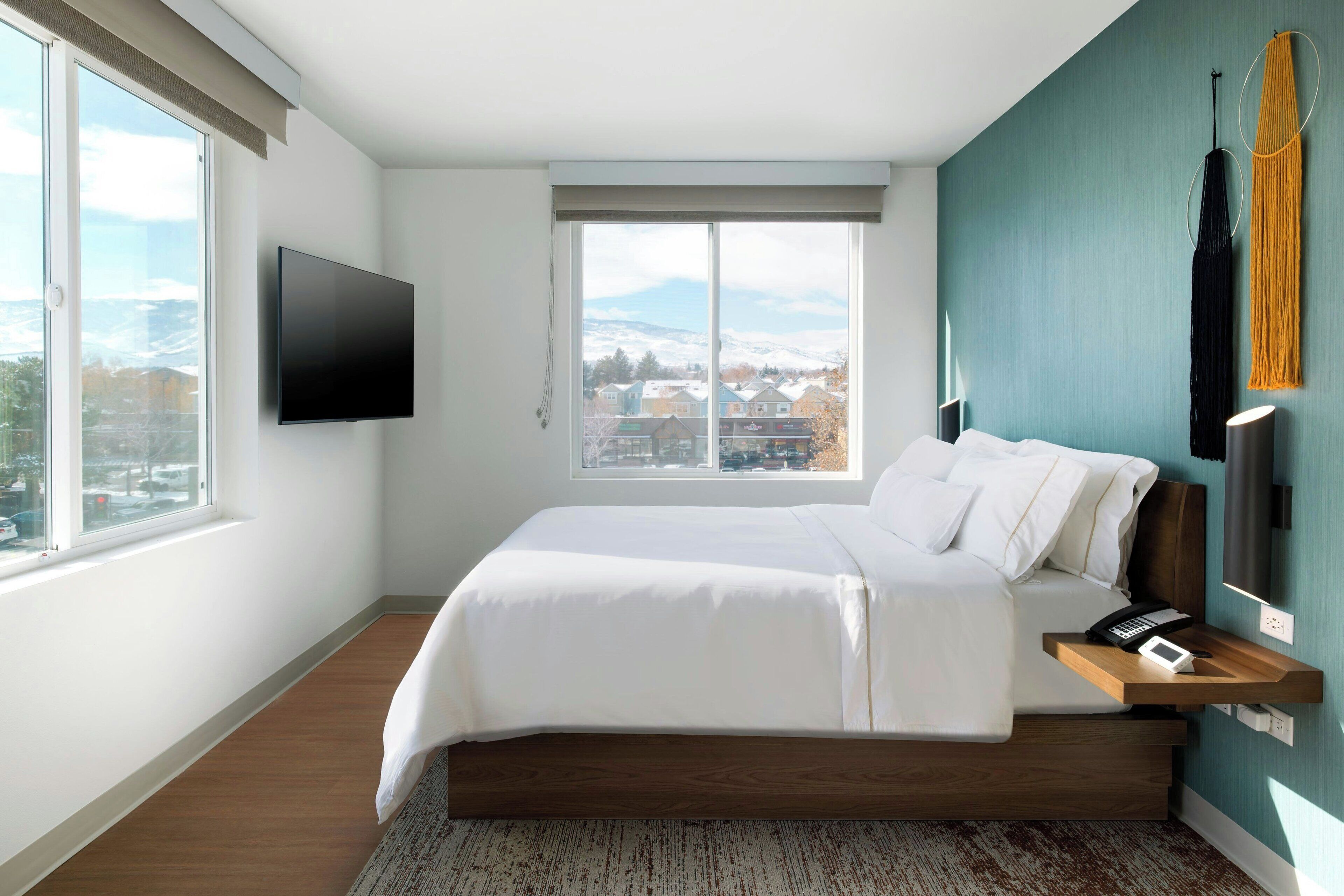 A modern bedroom with a large bed, a TV mounted on the wall, and a view of a snowy landscape through the window.