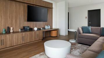 Een moderne woonkamer met een houten kast, een flatscreen televisie, een ronde witte salontafel en een hoekbank.