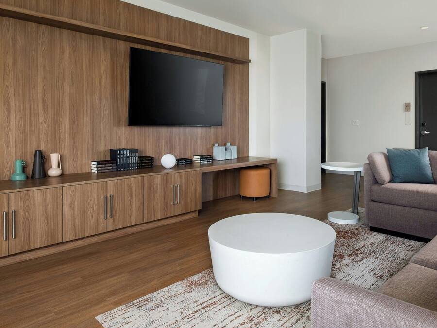 Een moderne woonkamer met een houten kast, een flatscreen televisie, een ronde witte salontafel en een hoekbank.