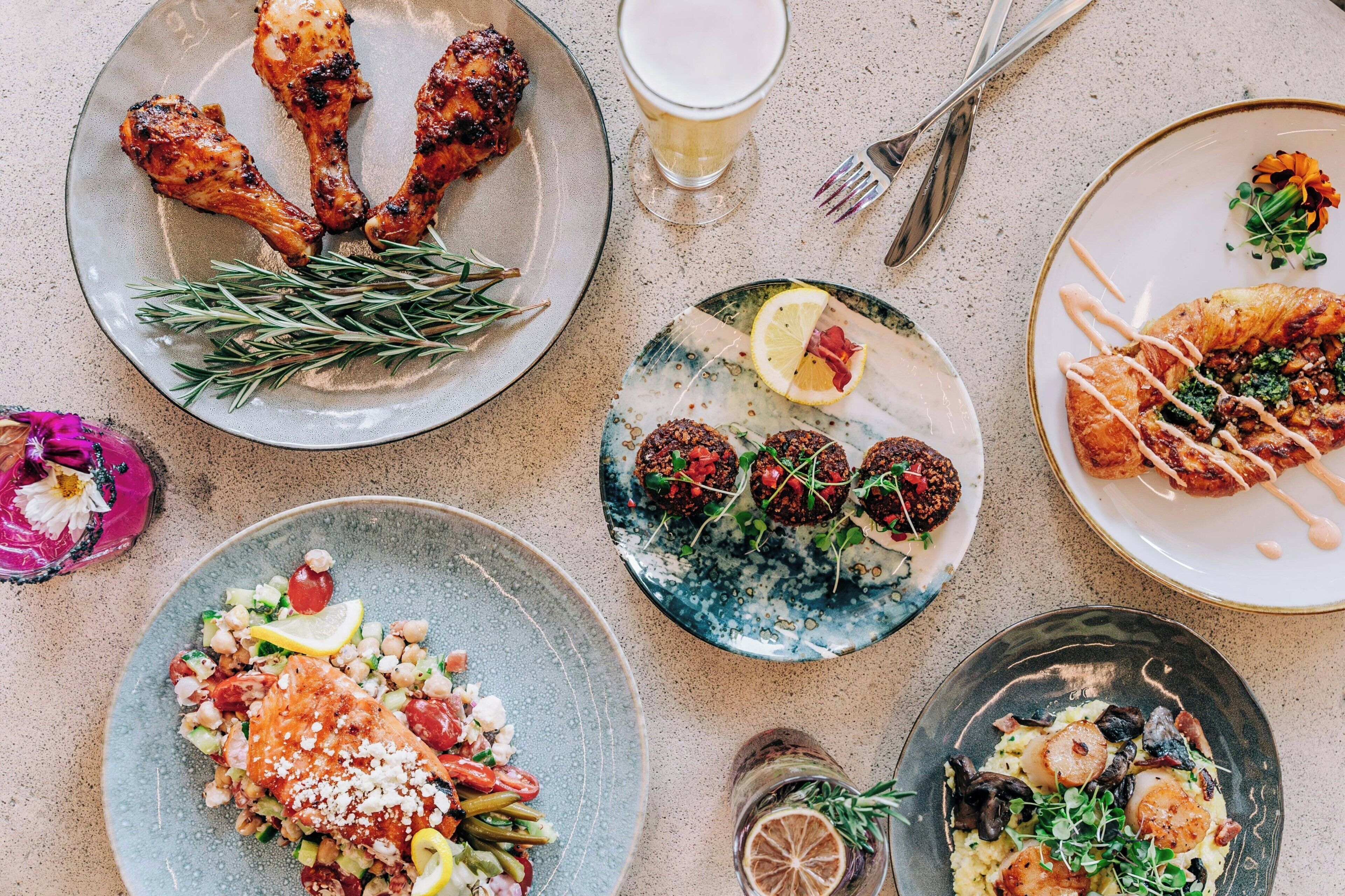 Uma mesa com diversos pratos, incluindo frango grelhado, salada e um croissant.
