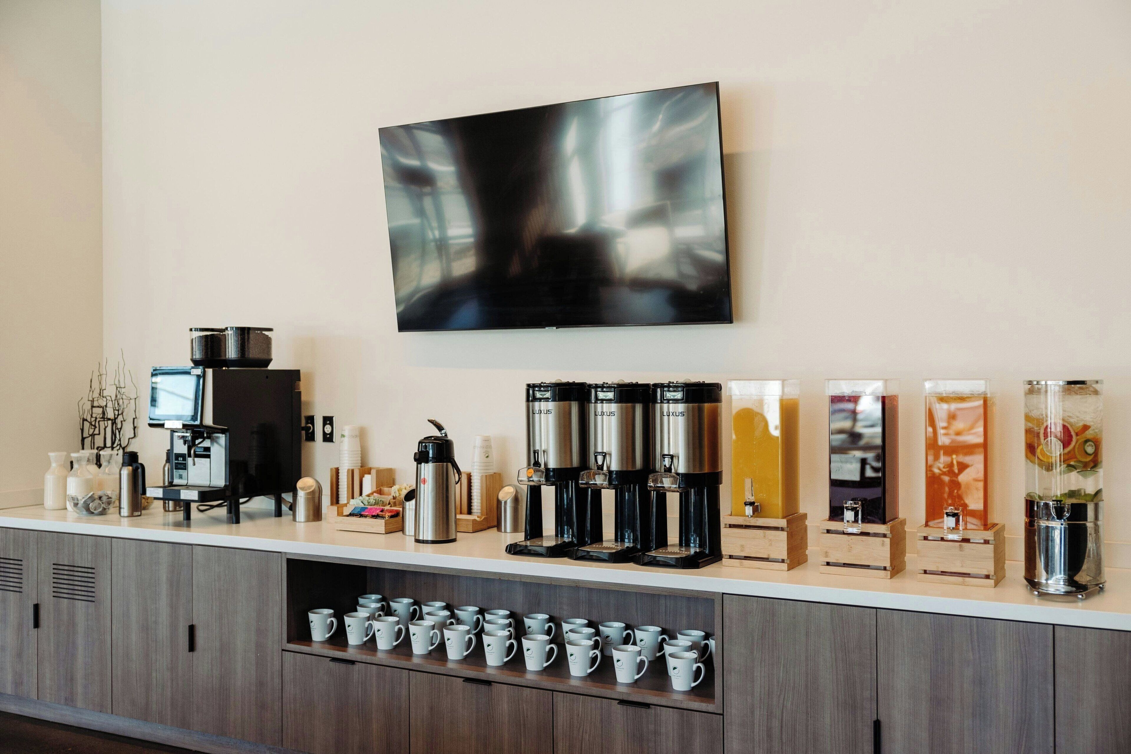 Un espace café moderne, équipé de plusieurs machines à café et d’un téléviseur à écran plat fixé au mur.