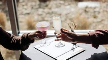 Two people holding glasses of drinks at a table with a view of a rocky landscape through a window.