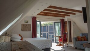 Un dormitorio con una cama grande, techo de madera, una mesita pequeña, una silla roja y vistas al exterior.