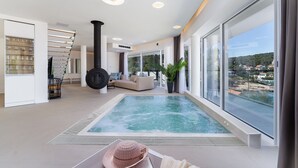 Area piscina interna moderna con vista sul mare, una scala e un angolo relax con divano e pianta in vaso.