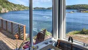 A deck with a wooden railing, a small table with a chair, and a view of a lake with a distant island. - Beautiful home in Farsund with WiFi (Farsund)
