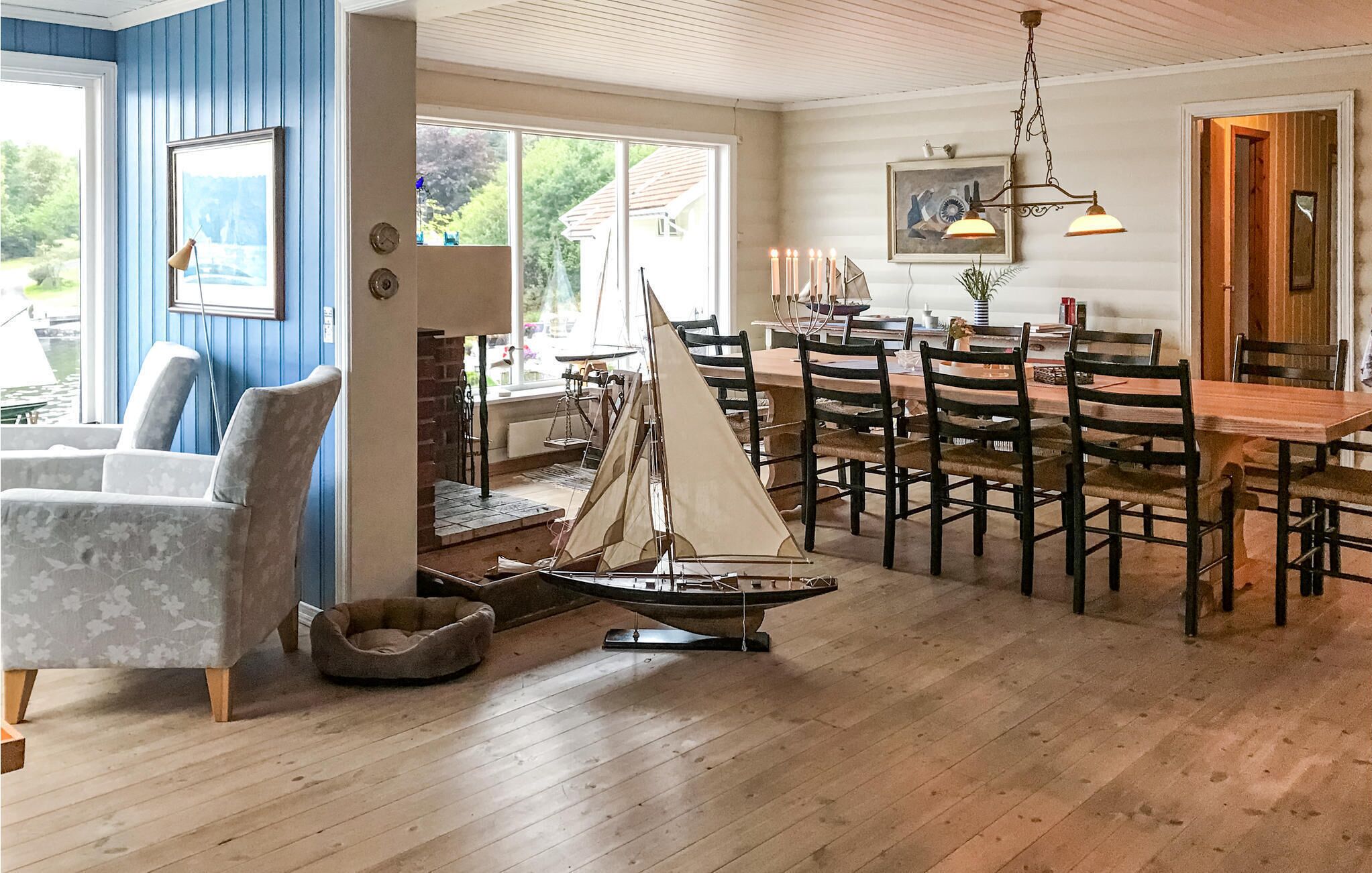 Comedor con mesas y sillas de madera, una maqueta de un velero y un ventanal con vista a la vegetación.