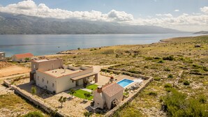 Una casa moderna con piscina, rodeada por un muro de piedra y vistas a un lago y montañas.