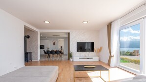 Una sala de estar moderna con un televisor grande, un sofá, una mesa de centro y vista al mar a través de un ventanal amplio.