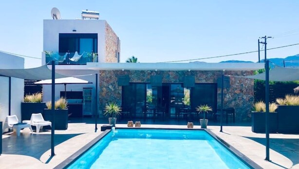 Un espace piscine extérieur moderne, avec une piscine à l’eau d’un bleu limpide, entourée de chaises longues et de plantes en pot.