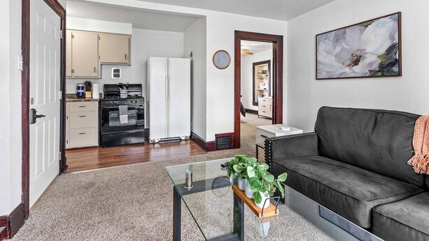 A living room with a dark grey sofa, a glass coffee table with a plant, and a painting on the wall. - The Tiny Piney - Live. Work. Play. Downtown Green Bay! (Green Bay)
