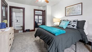 A bedroom with a bed, a desk, a chair, a dresser, and a ceiling fan. - The Tiny Piney - Live. Work. Play. Downtown Green Bay! (Green Bay)
