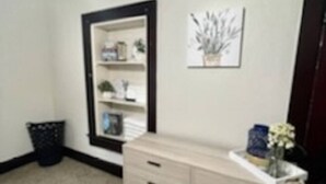 A room with a light-colored dresser, a small trash can, and a framed picture on the wall. - The Tiny Piney - Live. Work. Play. Downtown Green Bay! (Green Bay)