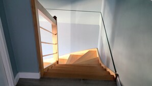 Un escalier avec des marches en bois et une rampe en verre, menant à un palier où se trouve un luminaire.