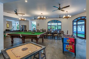 A spacious indoor recreational area with a pool table, foosball table, and multiple ceiling fans.